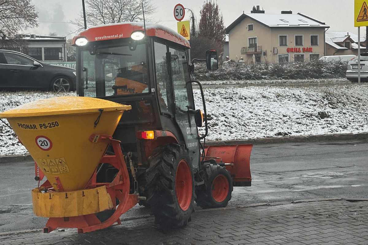 Traktor z piaskarką podczas zimowego odśnieżania i posypywania chodników w Lublinie