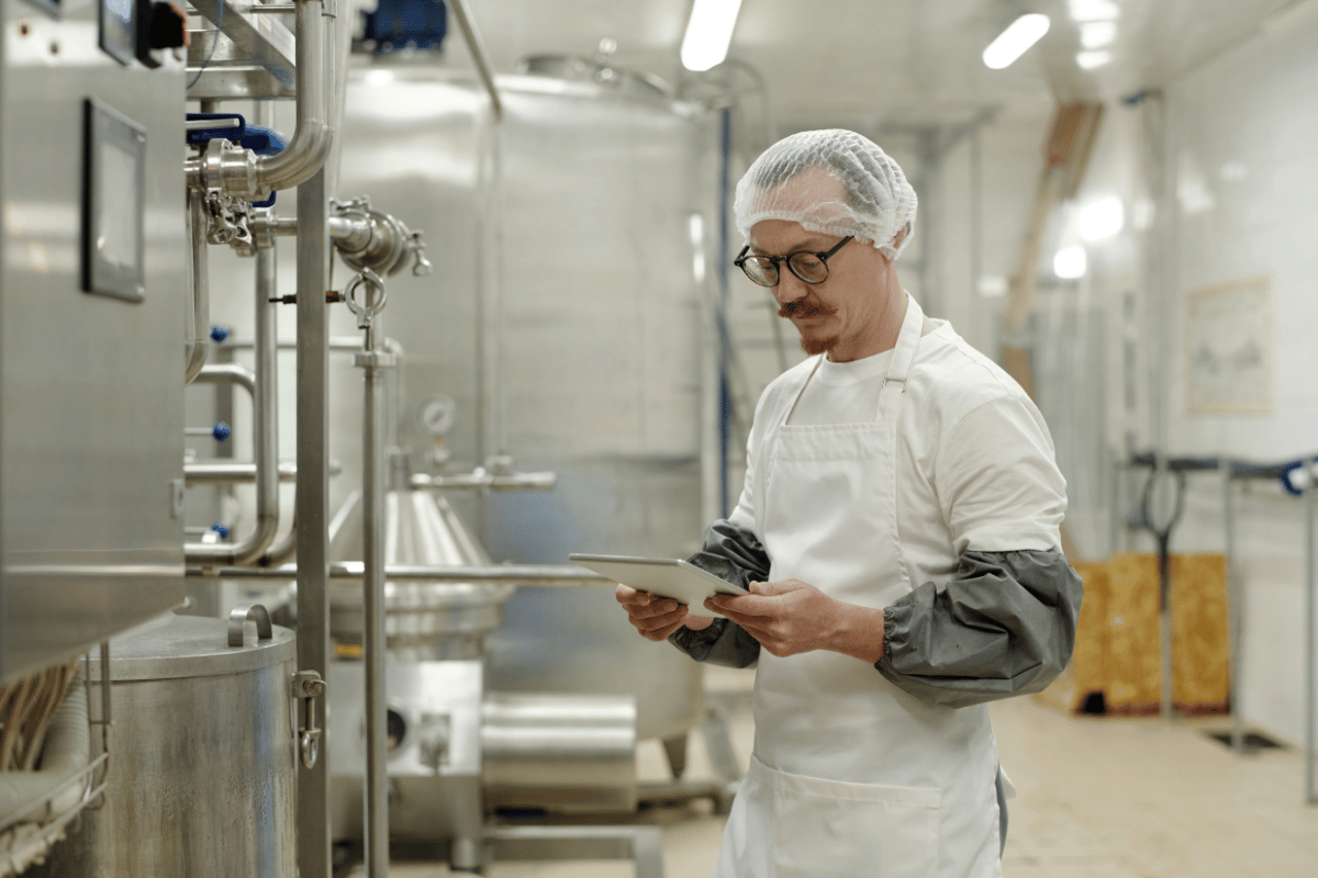 Pracownik w czepku ochronnym kontroluje dokumentację higieny w hali produkcyjnej