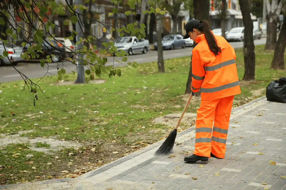 Pracownik sprzątający chodnik i teren zewnętrzny przy drodze