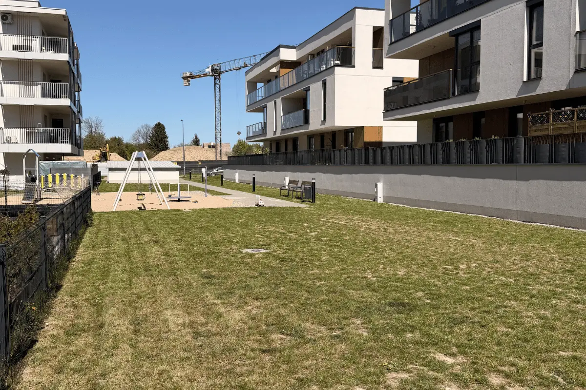 Plac zabaw na osiedlu mieszkaniowym otoczony pielęgnowaną zielenią i trawnikiem