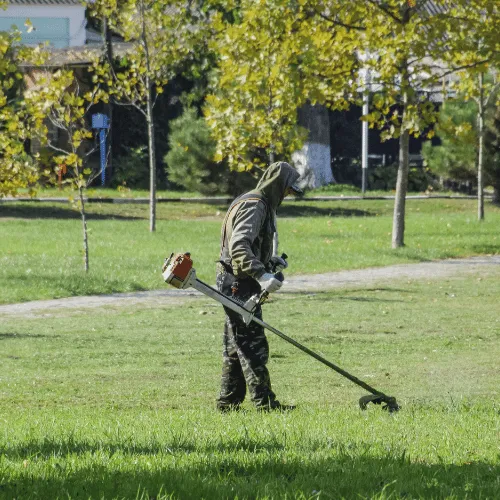Pracownik kosi trawę podkaszarką na terenie osiedla mieszkaniowego