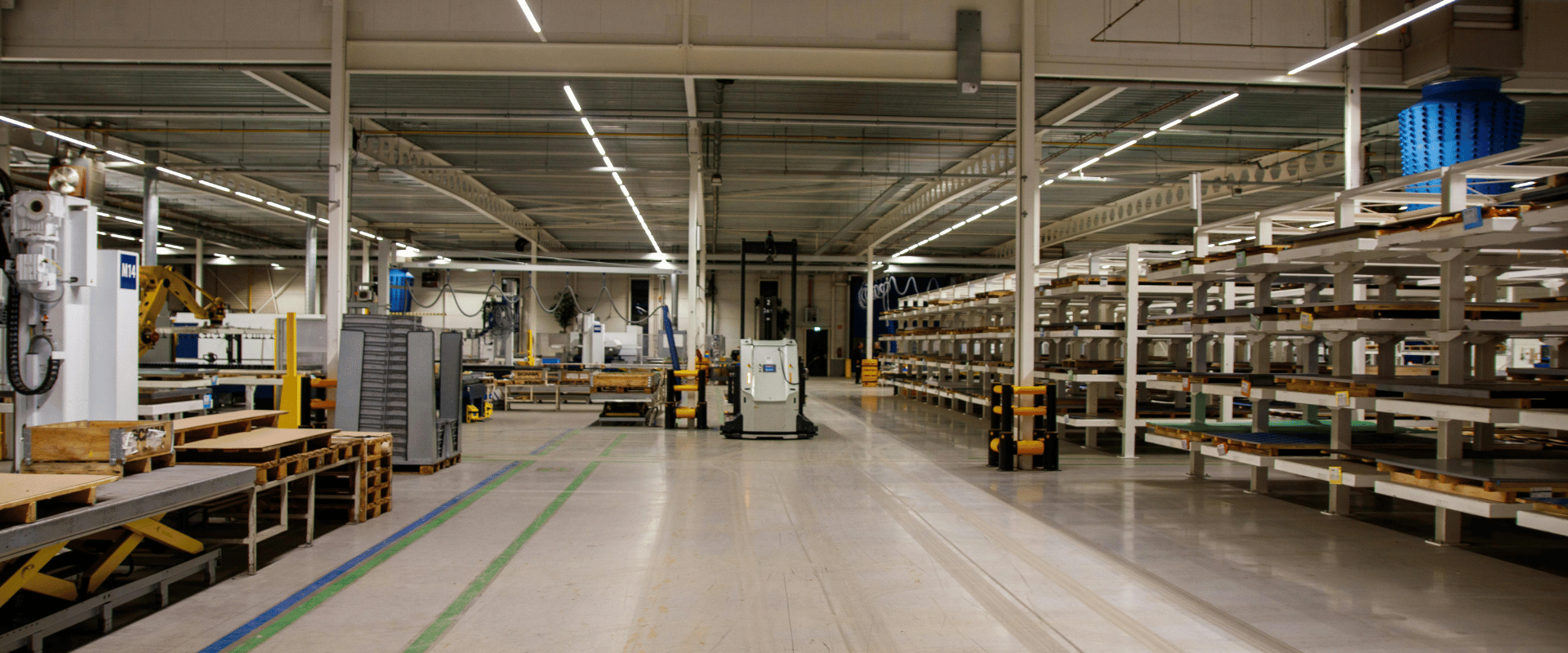 Czysta hala produkcyjna z linią technologiczną i regałami magazynowymi – przemysłowe sprzątanie hal i utrzymanie porządku.