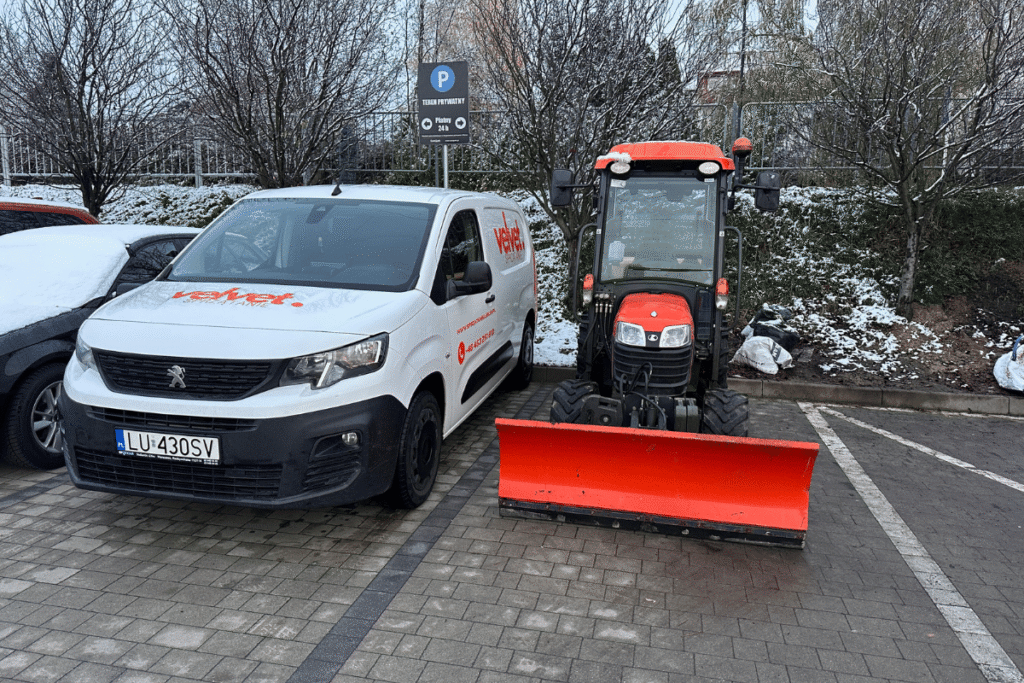 Flota Velvet Sprzątanie – samochód firmowy i ciągnik z pługiem do odśnieżania zaparkowane na osiedlu