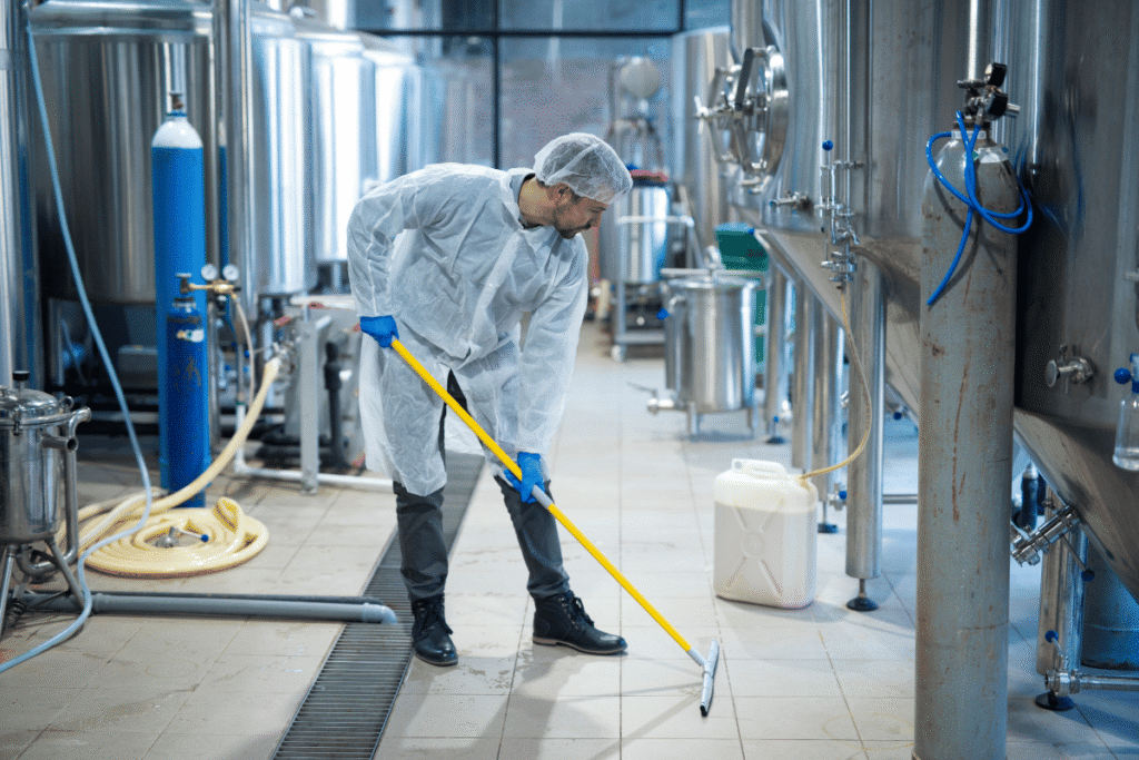 Pracownik w kombinezonie ochronnym myje posadzkę w zakładzie przemysłowym – higieniczne sprzątanie hali produkcyjnej