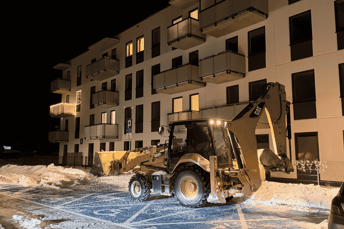 Nocne odśnieżanie parkingu na osiedlu w Lublinie koparko-ładowarką i sprzętem do odśnieżania