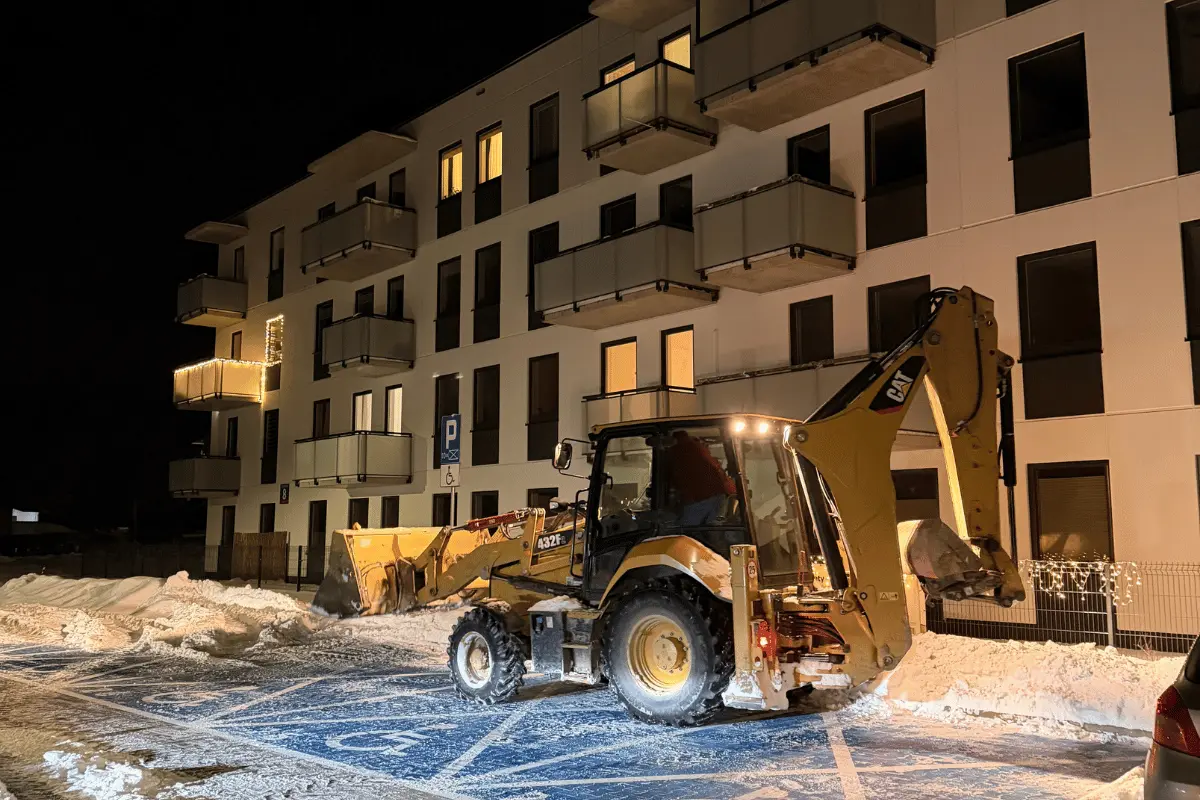 Koparko-ładowarka podczas odśnieżania parkingu osiedlowego nocą