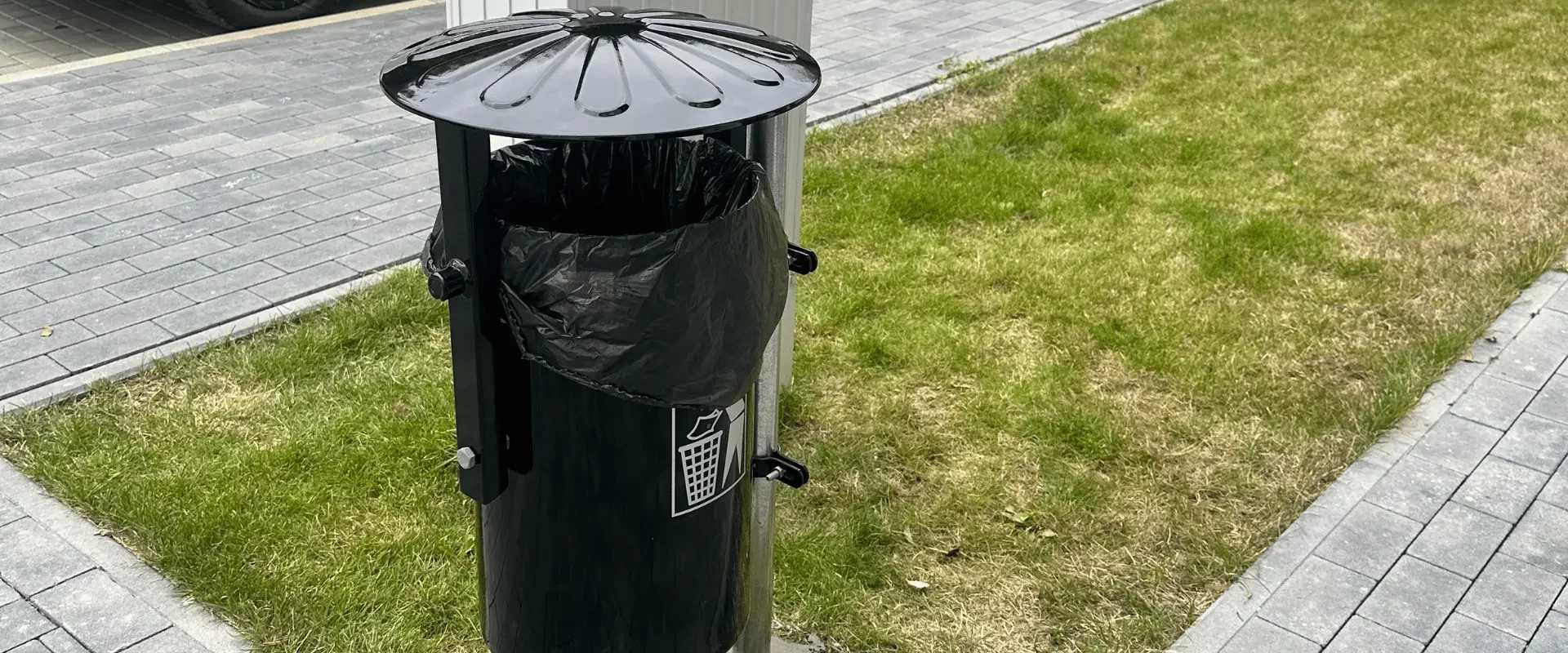 Kosz na śmieci na terenie osiedla mieszkaniowego przy zadbanych terenach zielonych