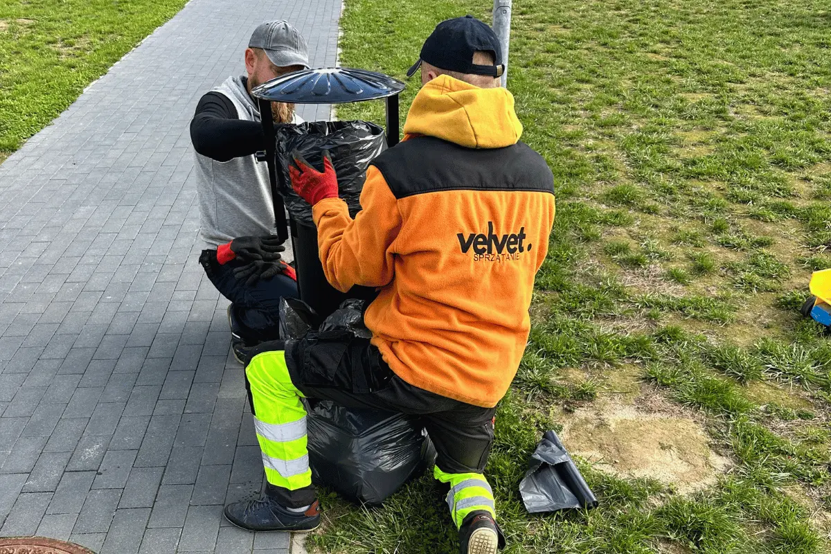 Pracownicy firmy sprzątającej podczas montażu i wymiany kosza na śmieci na osiedlu