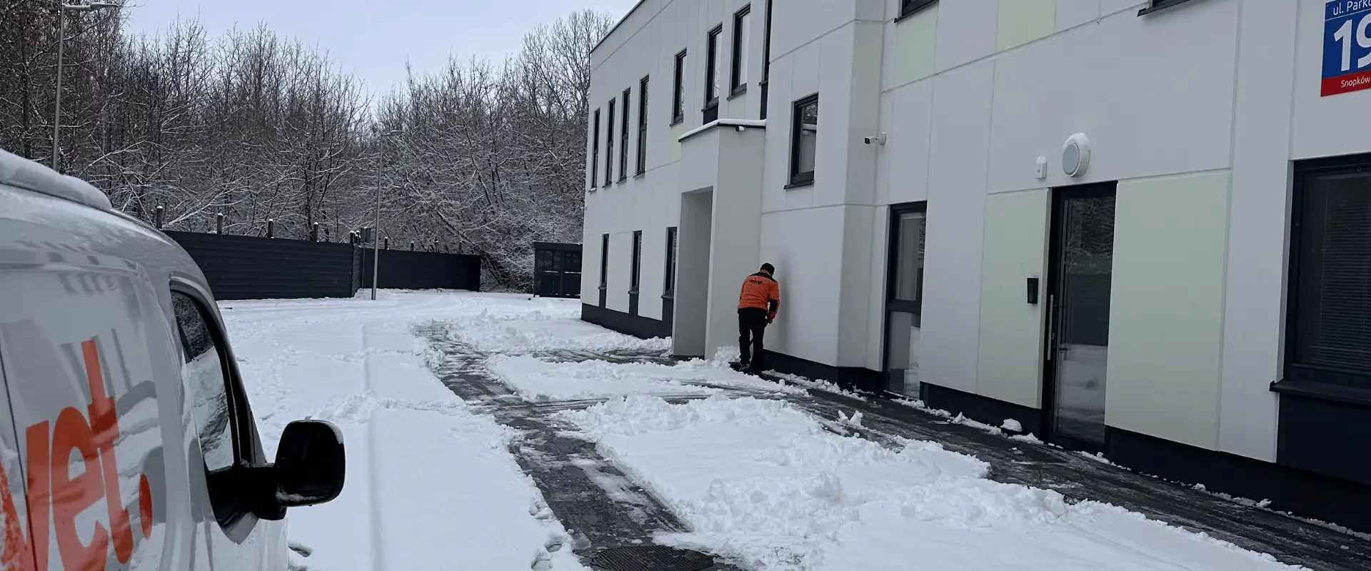 Pracownik firmy sprzątającej odśnieża teren wokół budynku firmowego zimą