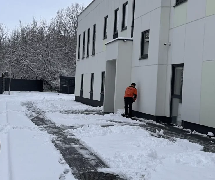 Pracownik firmy sprzątającej odśnieża teren wokół budynku firmowego zimą
