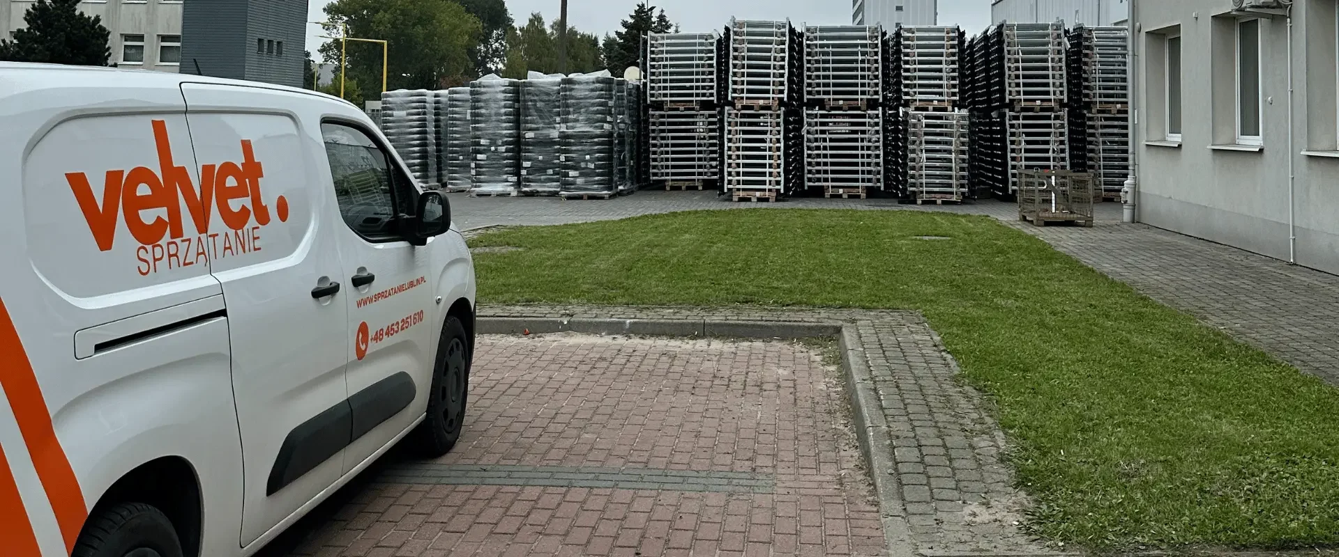 Samochód serwisowy Velvet Sprzątanie zaparkowany przy terenie zewnętrznym obiektu z utwardzonym parkingiem, trawnikiem i strefą magazynową w tle