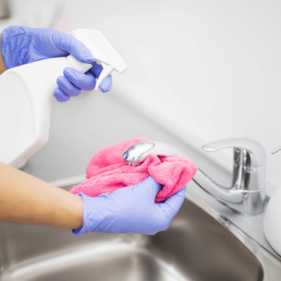 Dezynfekcja kranu w szkolnej łazience – rękawiczki, spryskiwacz i ściereczka z mikrofibry