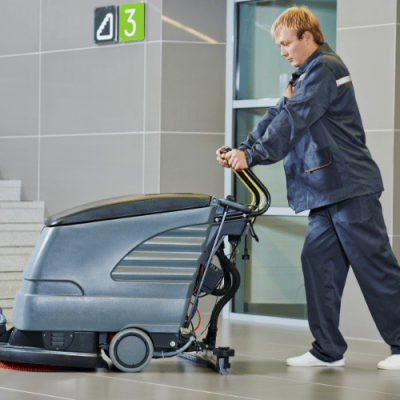 Maszynowe sprzątanie hal – operator prowadzi szorowarkę do posadzek w obiekcie przemysłowym